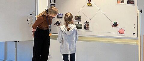 Das Foto zeigt die Studentin, die den Kakao-Workshop leitet, mit einer Schülerin vor dem Whitboard in einem Veranstaltungsraum des Botanischen Gartens.