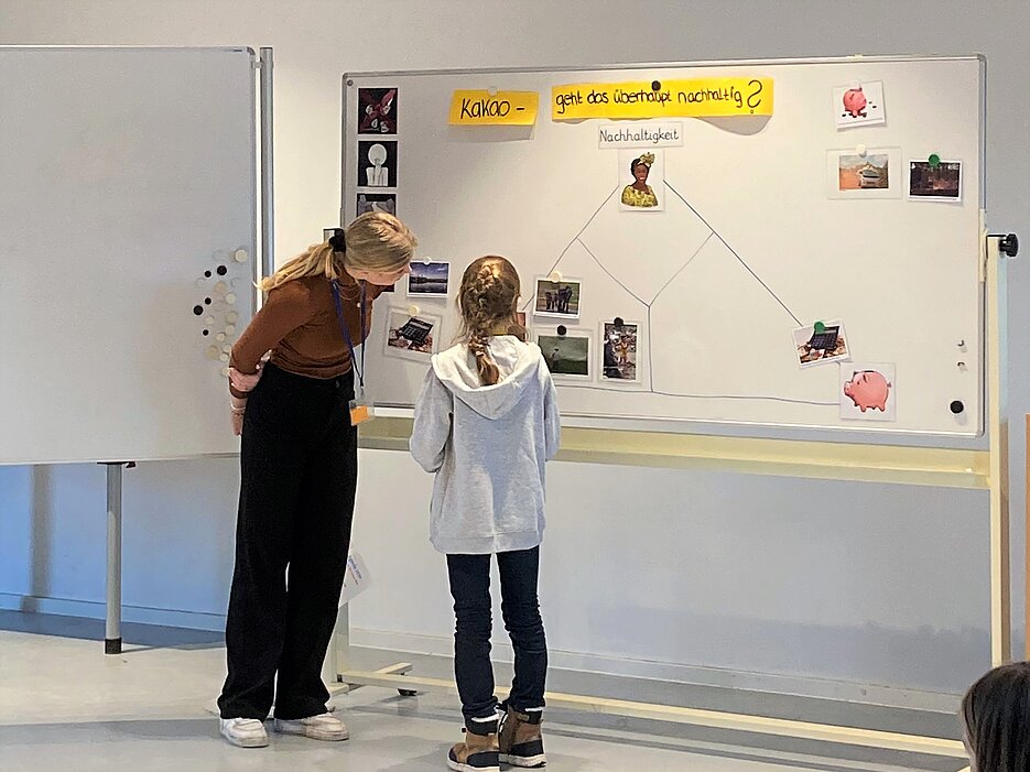 Das Foto zeigt die Studentin, die den Kakao-Workshop leitet, mit einer Schülerin vor dem Whitboard in einem Veranstaltungsraum des Botanischen Gartens.