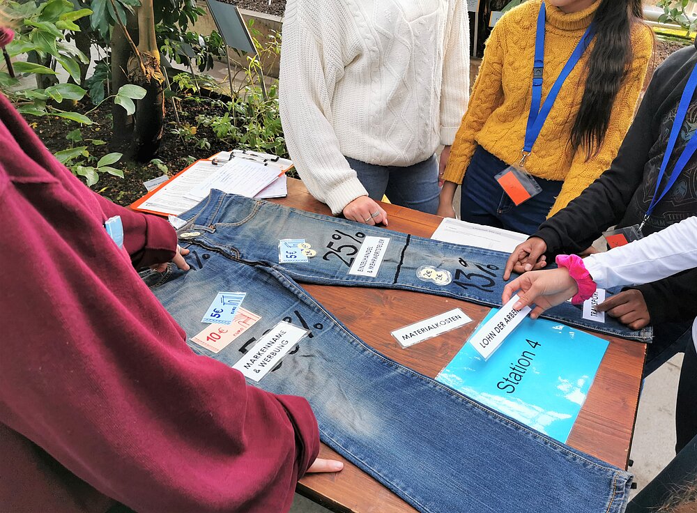 Auf dem Foto erarbeiten Studierende mit Schüler:innen die Wertschöpfungskette einer Jeans.